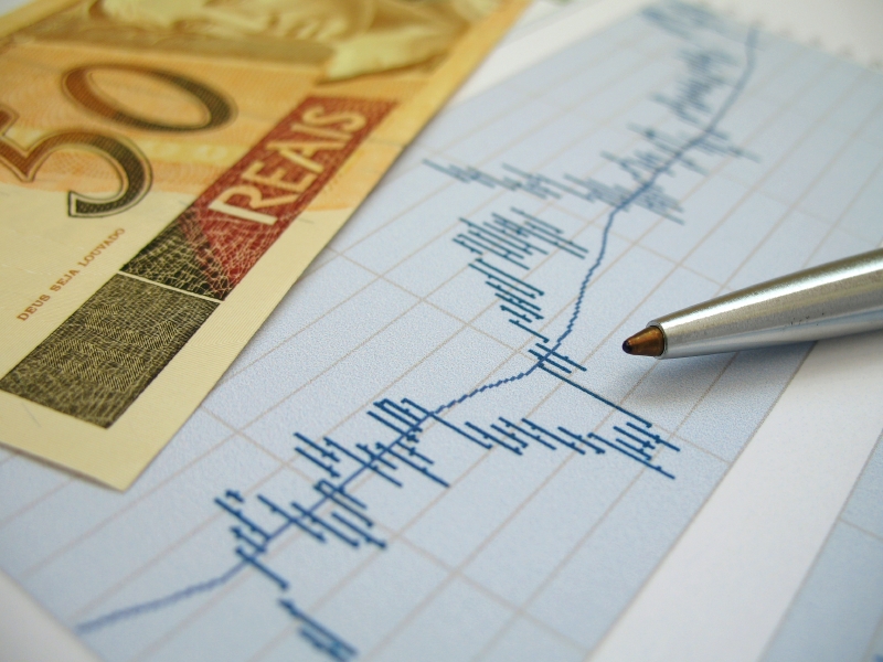 Stock Market Charts For Investor Analysis, With Brazilian Real $50 Bills And Pen, Using Selective Focus On Graph And Pen.